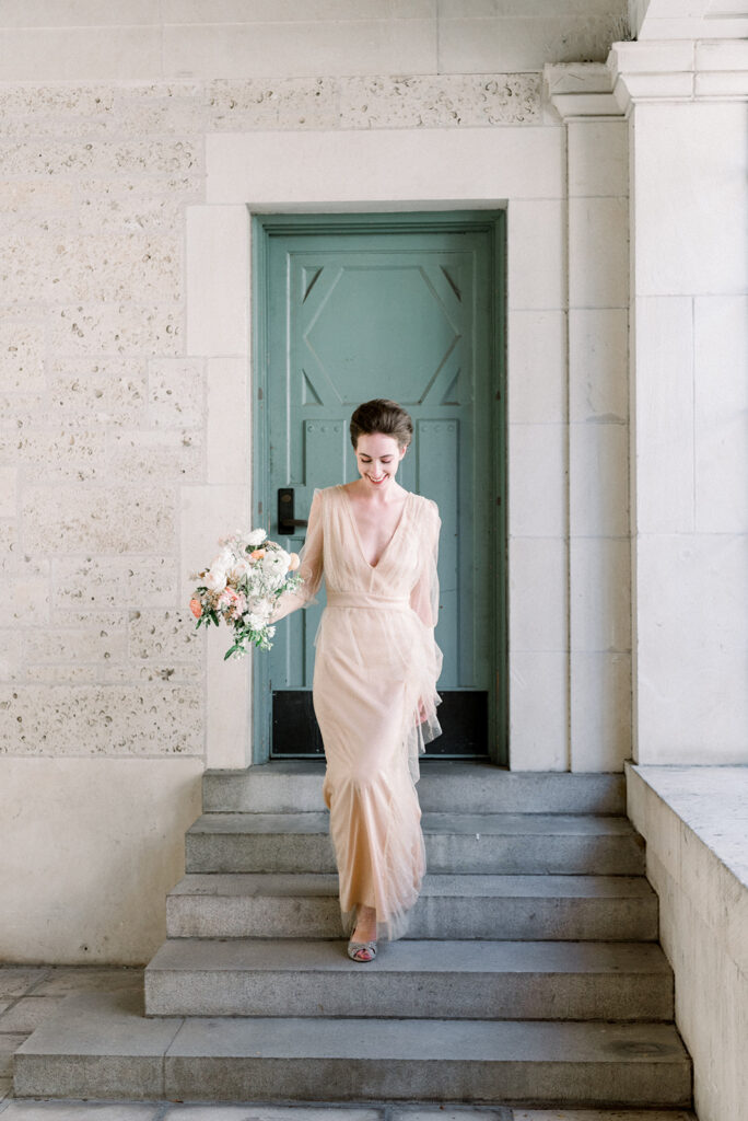 bride in guazy pink gown walks down the stairs with bouquet