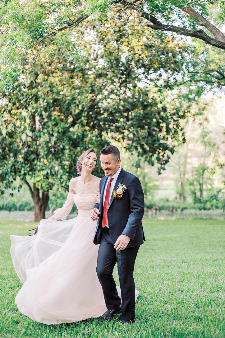 bride and groom walk through field, laughing